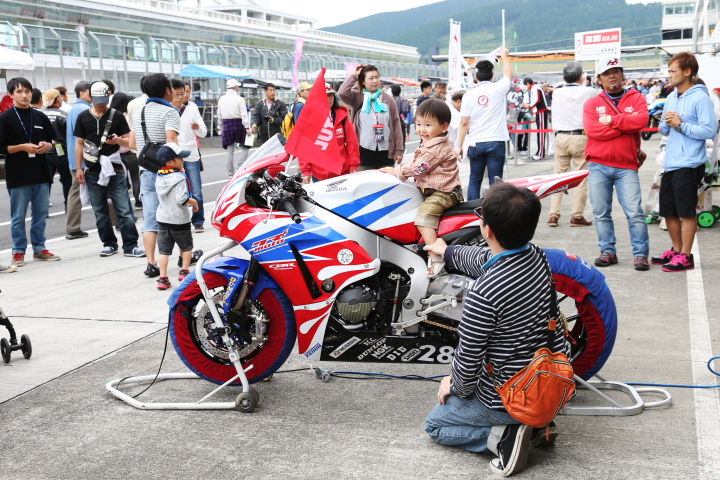 ピットウォーク: 2輪のレーサーにまたがり不安顔の子供と支えるお父さん